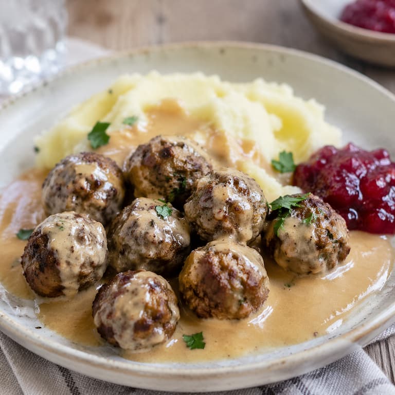 Veganska köttbullar med gräddsås, potatismos och lingonsylt på tallrik